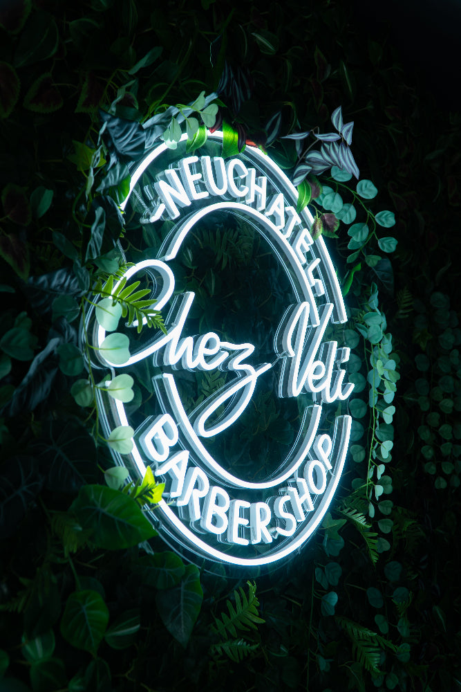 Enseigne néon verte et blanche Chez Lili Barbershop entourée de feuillage