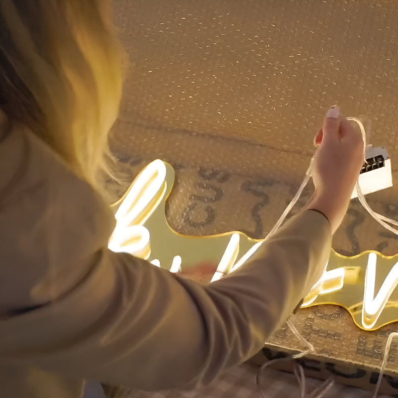 Femme installant un néon mural lumineux jaune dans une chambre