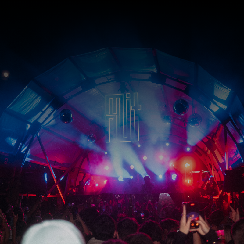 Scène de concert avec jeux de lumière et enseigne néon, ambiance festival nocturne